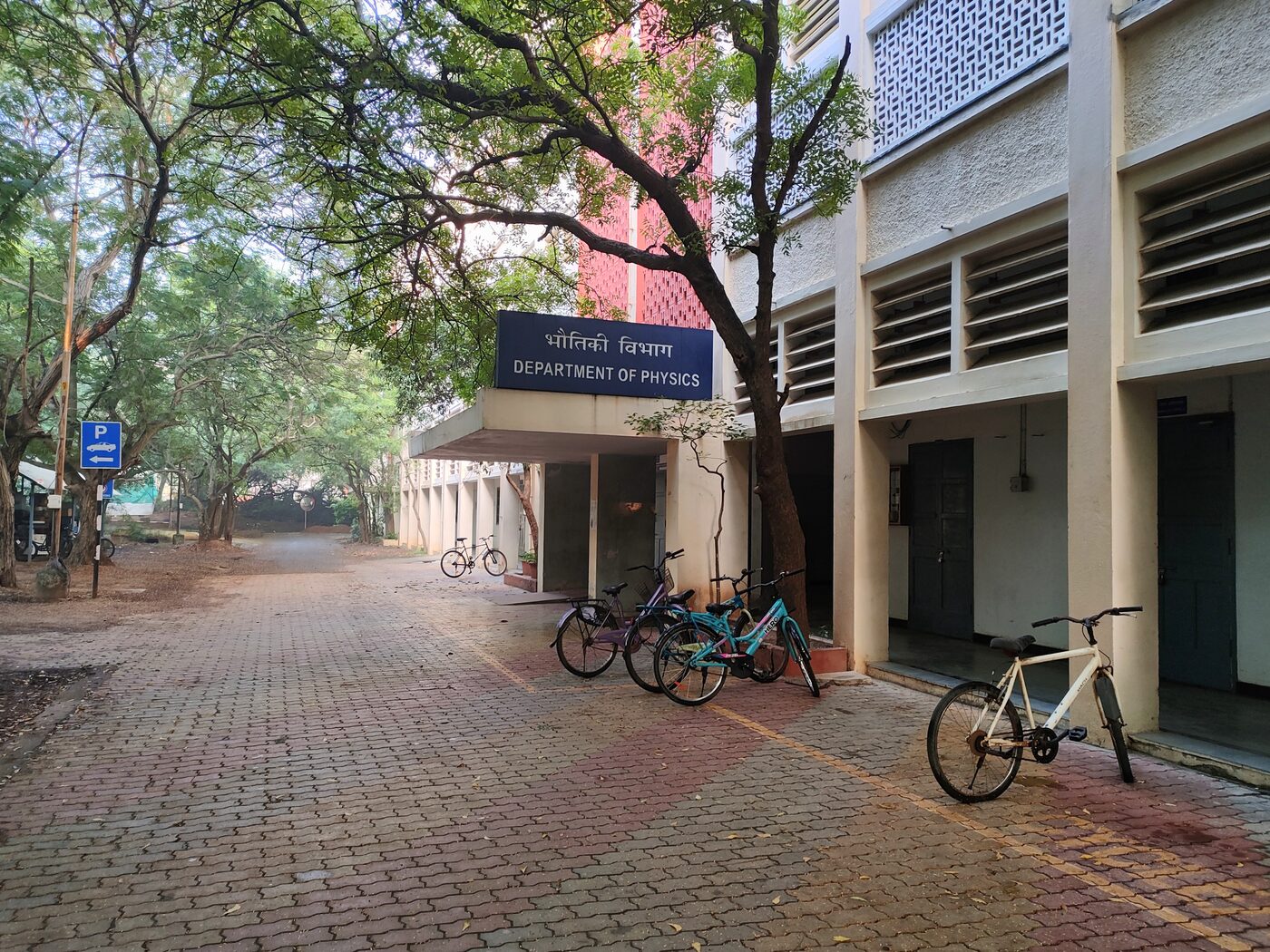 The entrance to the Department of Physics at IIT Madras, its sign in Hindi and English, with bicycles parked along the tree-lined path outside