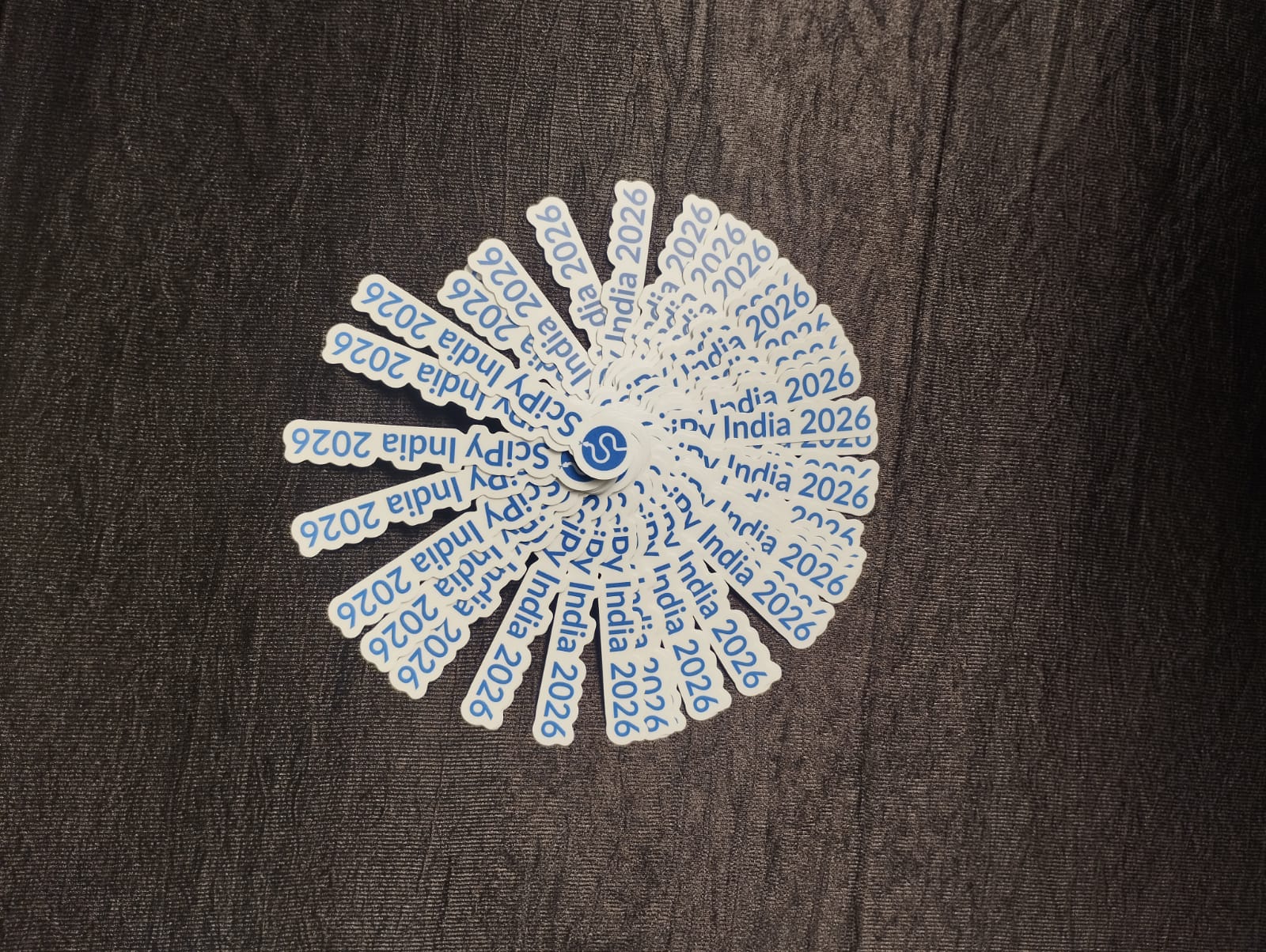 A fan of SciPy India 2026 stickers on a dark tablecloth