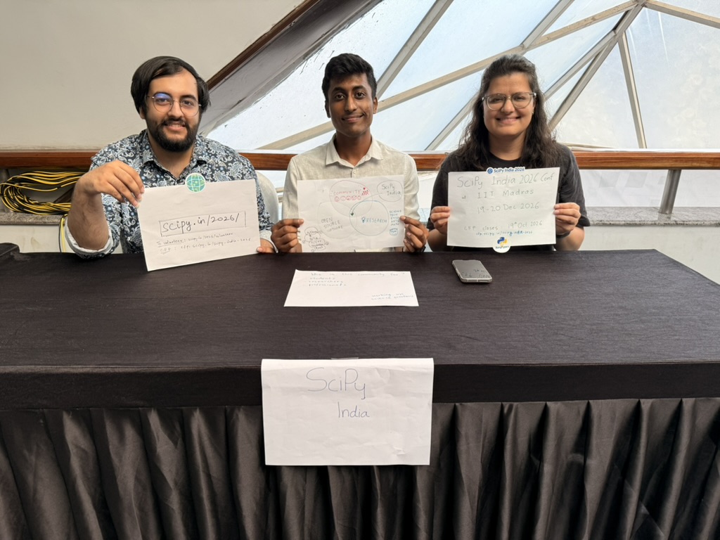 The SciPy India team at the booth, holding up the hand-drawn signs